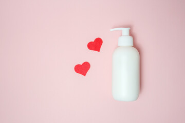 A bottle with a thick cream without a lid on a pink background, beside lie small hearts in red.