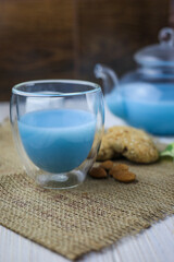 A glass cup and tea pot of blue Anchan Tea, cookies, milk,honey,almond.