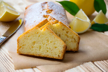 Loaf of gluten free lemo cake with pieces of lemon, green leaves and knife on rustic wooden background. Slice of citrus pie by classic recipe. Healthy nutrition, homemade vegan dessert.