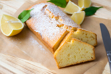 Loaf of gluten free lemon cake with sugar powder, pieces of lemon, green leaves  on rustic wooden background. Close up slice of citrus pie by classic recipe. Healthy nutrition, homemade vegan dessert.