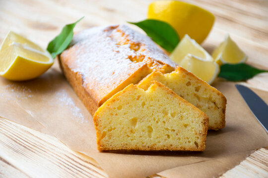 Loaf of gluten free lemon cake with sugar powder, pieces of lemon, green leaves  on rustic wooden background. Close up slice of citrus pie by classic recipe. Healthy nutrition, homemade vegan dessert.