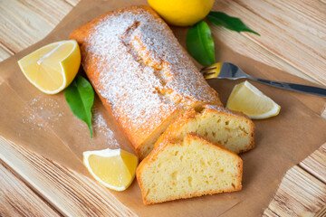 Loaf of gluten free lemon cake with sugar powder, pieces of lemon, green leaves  on rustic wooden background. Close up slice of citrus pie by classic recipe. Healthy nutrition, homemade vegan dessert.