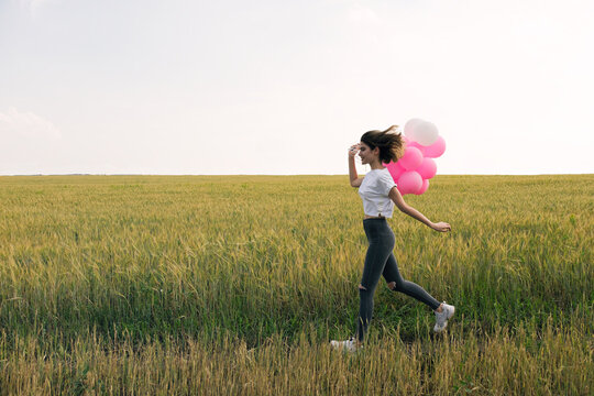 Happy young girl with air balloons running against of field