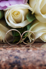 Wedding rings on granite stand against the background of a beautiful bouquet of flowers