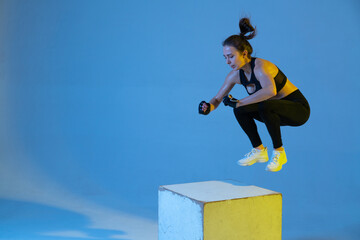 Young sportive woman jumping on cube. Neon light in studio.