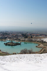Lake, thermal pool near geothermal springs of Pamukkale, surrounded by travertines, white mountains and taking off, flying hot air balloonin sunny weather in bright afternoon. Turkey national landmark