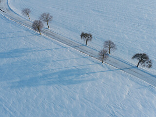 Luftbild einer Straße im Schnee mit Schatten von Bäumen
