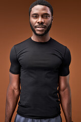 confident sportsman looking at camera isolated on brown background, handsome bearded male in black sportive t-shirt