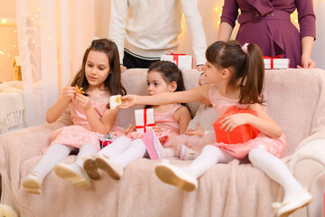 family portrait of a parents and children, sitting on a couch in home interior decorated with lights and gifts