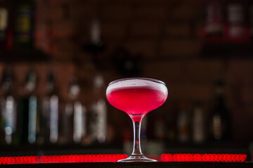 Classic Pink Lady cocktail closeup with flower and cherry on bar counter