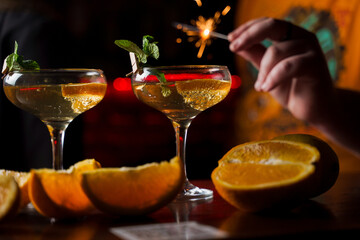 Celebrating new year eve 2022 with sparklers fireworks and drinking cocktails. Mint with orange slice in a cocktail glass filled with alcohol cocktails.