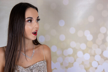 A sexy elegant woman wearing a silver glittery party dress with long brown hair and red lipstick and a diamond necklace looking like she is ready for an elegant Christmas party or wedding event