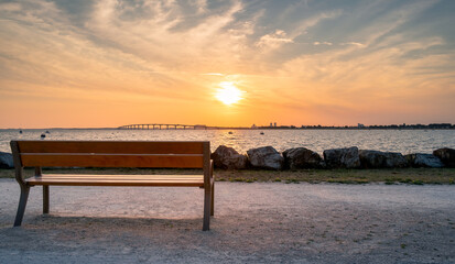 Isolated public bench at sunrise. Re island bridge in the background