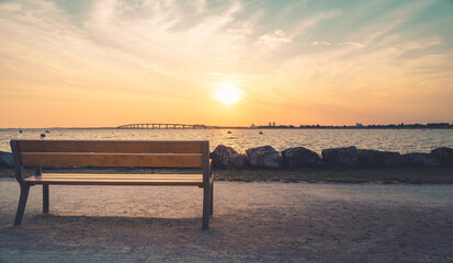 Isolated public bench at sunrise. Re island bridge in the background