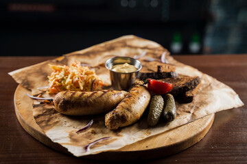 Grilled sausages with beer and vegetables with pickled cucumber, cabbage salad sauce and bread on parchment, top view.