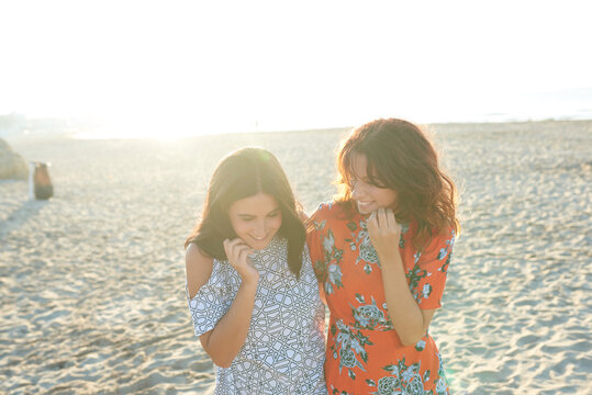 Two smiling happy girlfriends walking on beach in sunrise