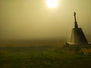 Dark blurred cross in fog field. Rising Sun. Post background with vignettes and copy space for text