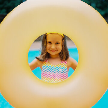 Cute young girl with a big inter tube standing by a swimming pool