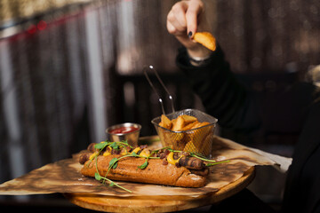 Barbecue grilled hot dog with yellow mustard and ketchup on wooden background. Hot dog sandwich with potato fries and sauces.