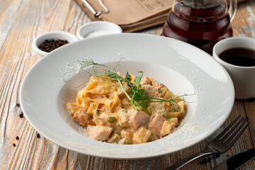 Carbonara creamy pasta with bacon crisps on a light wooden table in a restaurant