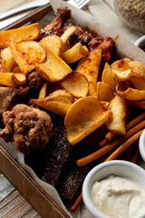 Beer snacks in a wooden tray: french fries, baked potato and chicken wings with sauces