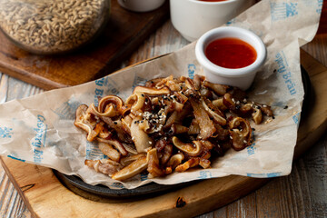 Gourmet pub snack roasted pork ears with garlic and chili sauce, served on wooden table, close up