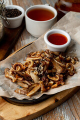 Gourmet pub snack roasted pork ears with garlic and chili sauce, served on wooden table, close up