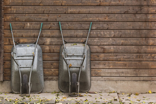 Two wheelbarrows leaning against the wall of a shed