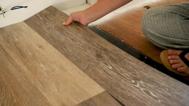 Woman connecting wood-like floor plank to other floor planks 2. Camera focuses on the woman&rsquo;s hands as they adjust laminate.