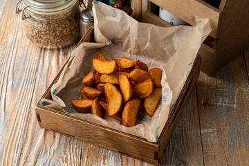 Beer snack in a wooden tray: baked potato segments with paprika, top view