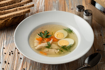 Simple chicken broth with egg and white meat, traditional treatment from cold and flu, served on rustic wooden table