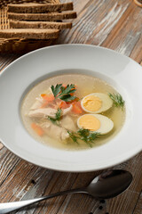 Simple chicken broth with egg and white meat, traditional treatment from cold and flu, served on rustic wooden table