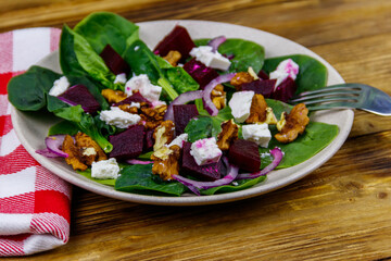 Tasty spinach salad with boiled beetroot, feta cheese, walnut and red onion on wooden table. Healthy vegetarian food