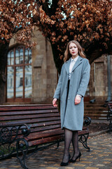 Beautiful fashionable woman with stylish clothes look in a gray classic coat walks on the street in yellow autumn foliage