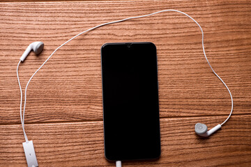 Smartphone and headphones on a rustic wooden table. Top view with copy space