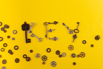 Steampunk photo. Word KEY written by different iron keys and gears laying around. Yellow background, top view