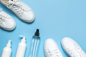 White leather sneakers, plastic bottles of cleaning products for shoes on blue background flat lay...