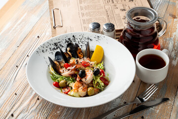 Mediterranean salad with mussels, shrimps and lettuce on a wide dish on a table