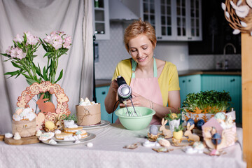 Beautiful young modern housewife cooks in the kitchen. portrait of a woman cook with mixer. Preparing for Easter cooking process. Confectioner's workplace. Hobby leisure relax. Digital detox. apron