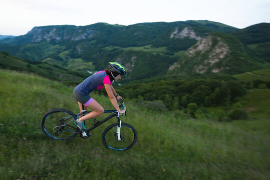 Caucasian young female riding mountain bike downhill a green mea