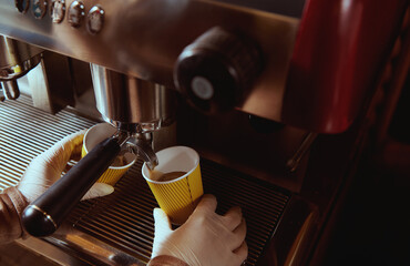 Coffee machine pourig coffee to yellow cardboard coffee cup in bar. Cropped image. Closeup
