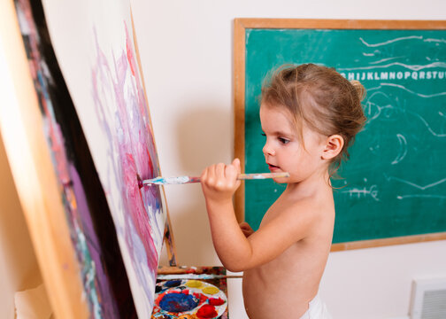 little girl painting at easle in diaper