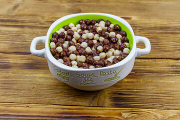 Cereal chocolate balls with milk in a bowl on wooden table