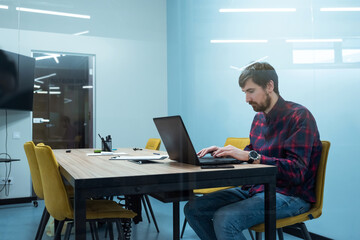 Young man working on a laptop sitting at his workplace in the office. Coworking, Business Concept
