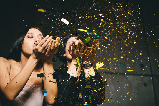 Two girls blowing golden confetti