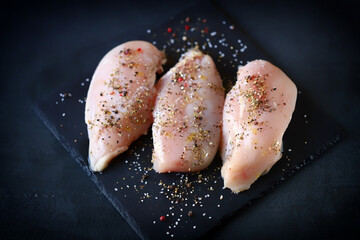 Selective focus. Raw chicken fillets with spices on a stone board.