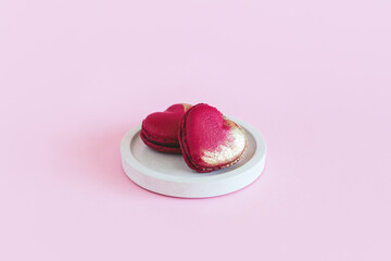 Heart-shaped macaroons on a white plate. Pink pastel background.  Concept for Valentine's Day.