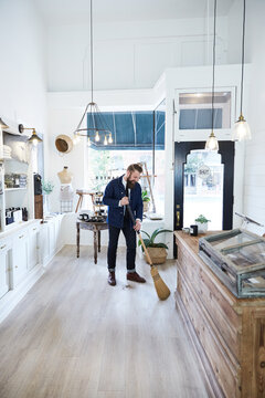 Millennial small business owner sweeping the floor in artisan retail shop