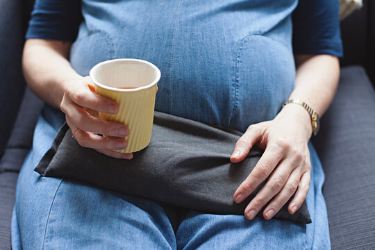 38 week pregnant women resting on couch with heat pack and herbal tea