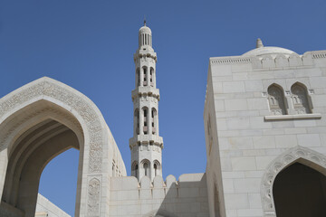 Fototapeta na wymiar Torbogen mit der arabischen Inschrift Große Sultan-Qabus-Moschee und dem Hauptminaret in einer Sichtachse . Sie gilt als eine der wichtigsten Bauwerke des Sultanats Oman. 